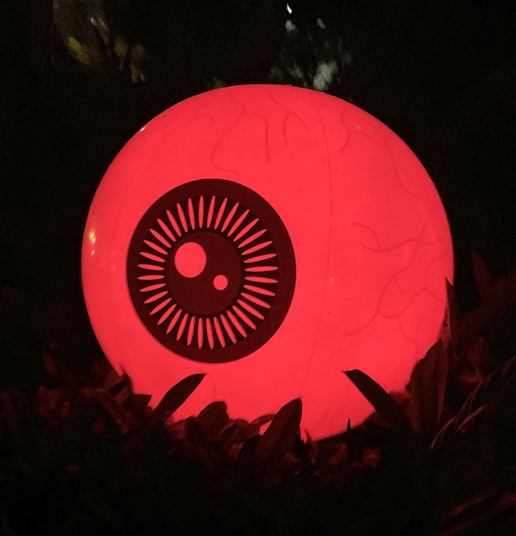 Glowing red inflatable eyeball with a black iris and vein details, pictured outdoors at night.