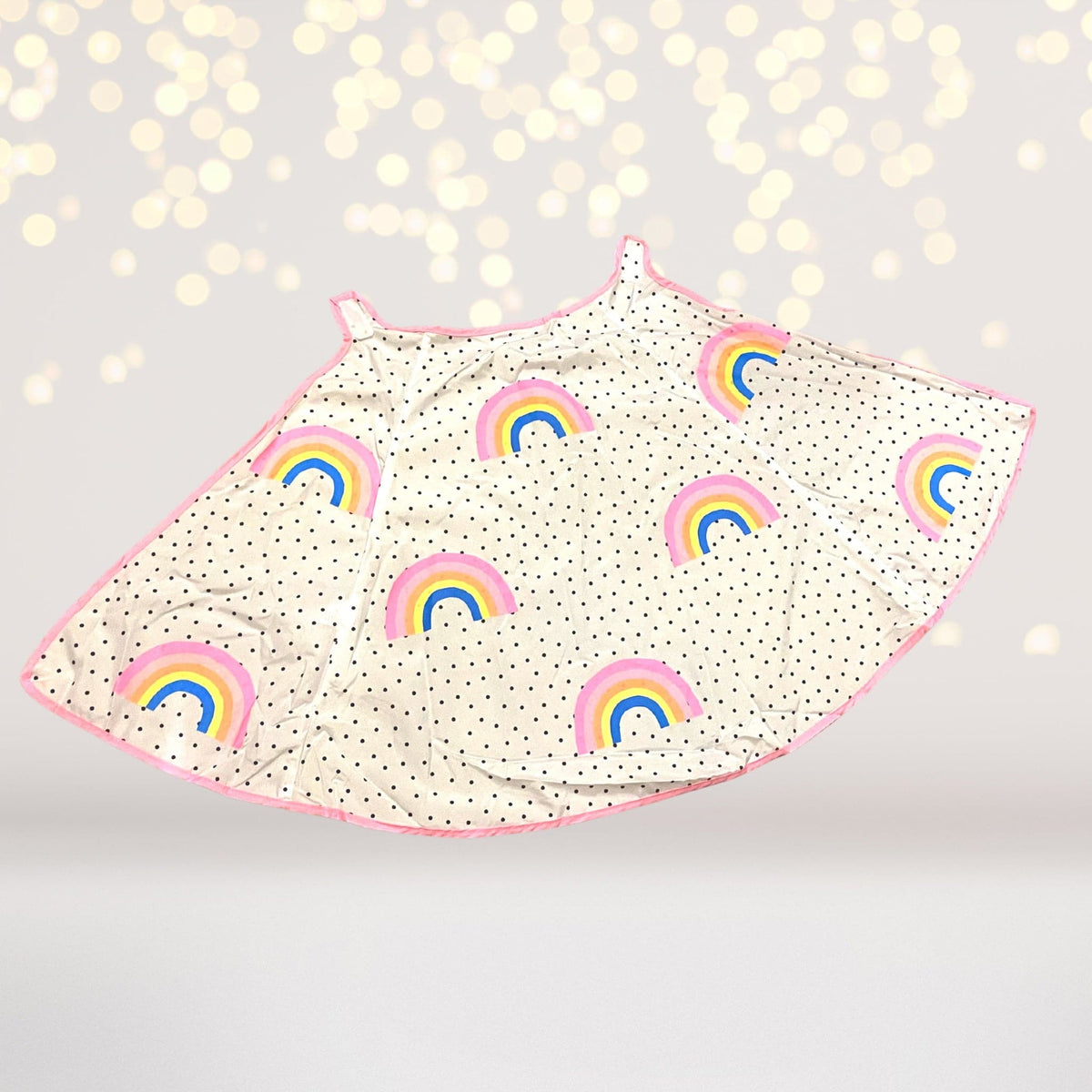 Light-colored children's costume cape printed with small rainbows and dotted details, with pink edging.