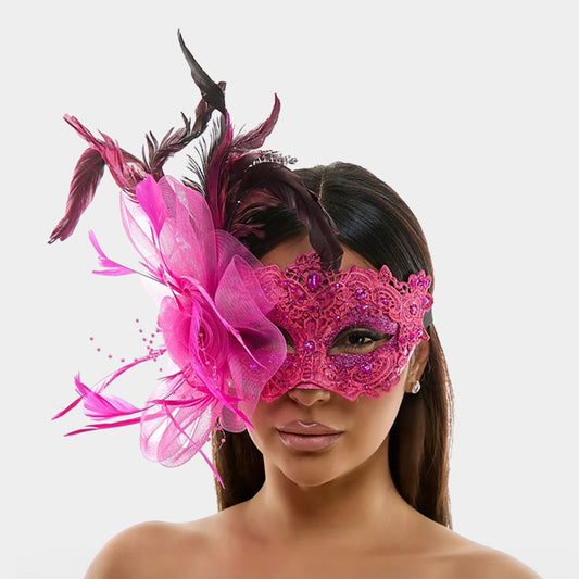 Pink lace masquerade mask with a large pink flower and pink and dark feathers, modeled on a face.